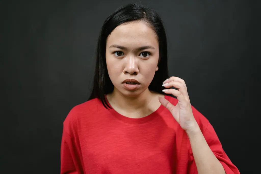 Portrait of an Asian woman in a red shirt against dark background expressing emotion.