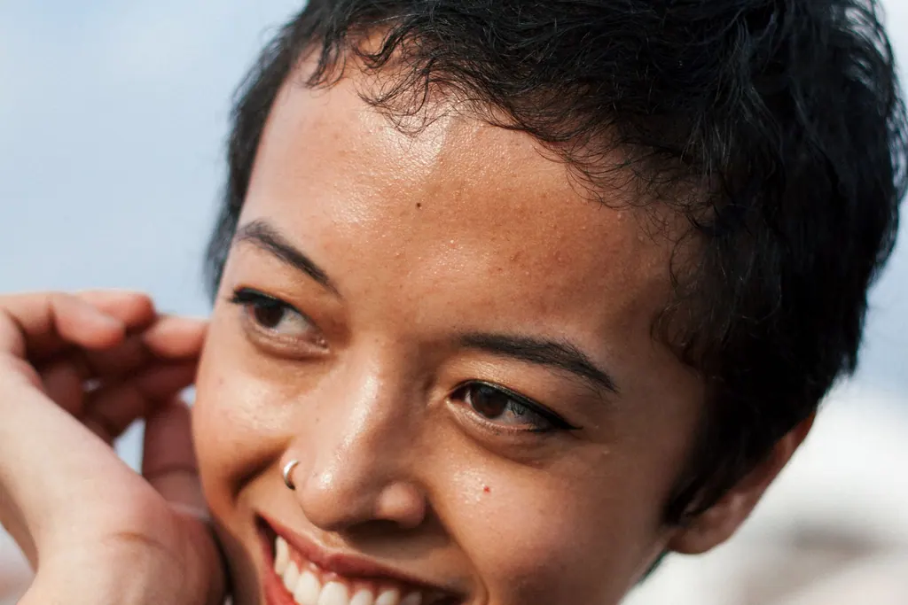 A cheerful woman with short hair smiling under the sun, showcasing natural beauty.